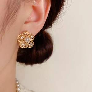 Detail of gold floral stud earring with a central pearl and micro-inlaid rhinestones