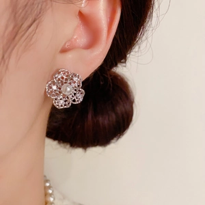 Detail view of silver hollow flower earrings with white pearl center on model