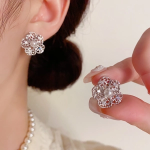Macro detail of silver hollow flower earrings with central pearl and zircon accents
