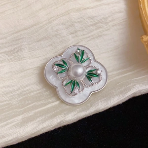 Detail of vintage flower brooch featuring white pearl, green enamel leaves and zircons