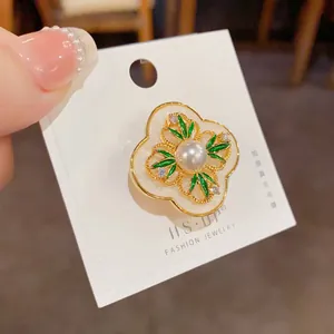 Detailed view of white four-leaf flower brooch with pearl and green leaf accents
