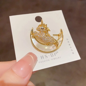 Détail d'une broche licorne dorée ornée de strass et base de lune en nacre naturelle