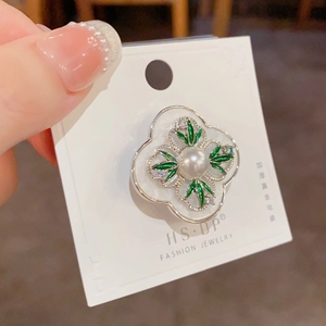 Macro detail of silver four-leaf clover brooch with green enamel and white pearl center