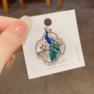 Detail of peacock brooch with blue enamel feathers and white crystals on card
