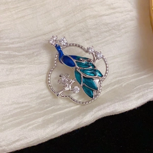 Elegant silver peacock brooch with blue enamel and sparkling crystals on a circular frame