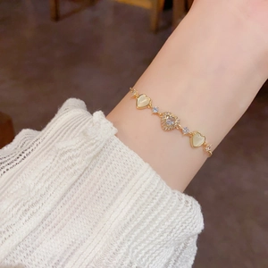 Detailed view of heart-shaped gold bracelet with zircons and cat's eye stones on wrist