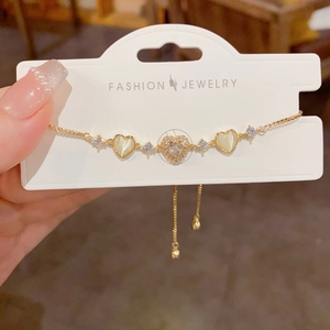 Adjustable gold bracelet featuring zircon heart and yellow cat-eye stone charms