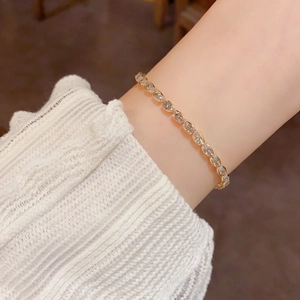 Elegant gold-tone oval crystal tennis bracelet worn on wrist with a stylish white cuff