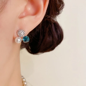 Nahaufnahme eleganter Ohrstecker mit Pavé-Diamanten, weißer Perle und blauem Kristall