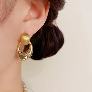 Nahaufnahme goldener geometrischer Ohrhänger mit mattiertem Stecker und polierter Schlaufe