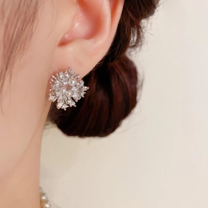 Detailed view of silver snowflake earrings with sparkling zircons and pearls on ear