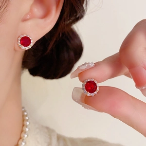 Détail d'une puce d'oreille halo dorée avec une gemme rouge et des zircons blancs