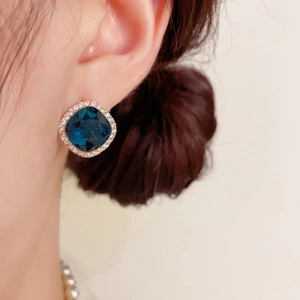 Détail de boucles d'oreilles carrées en zircon bleu avec design halo sur l'oreille