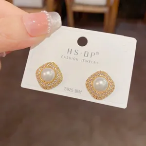 Detailed close-up of diamond-studded pearl earrings with S925 silver posts on a display card