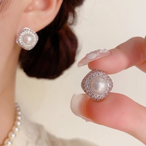 Close-up of silver rhombic stud earrings with central pearl and micro-set zircons on ear