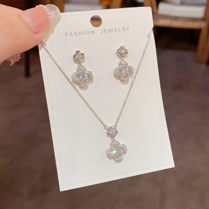 Detailed close-up of sparkling zircon four-leaf flower pendant necklace and earrings set