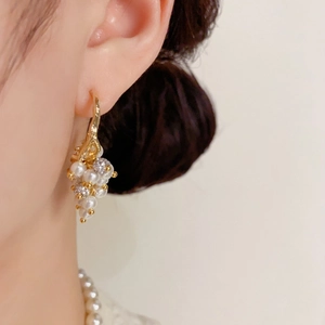 Close-up of elegant gold grape cluster earrings with white pearls and zircons on model