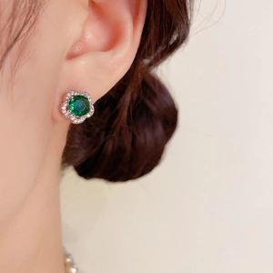 Gros plan sur un bouton d'oreille fleur avec gemme verte porté par un modèle