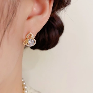 Détail d'une boucle d'oreille gourde dorée sertie de zircons brillants portée par un modèle