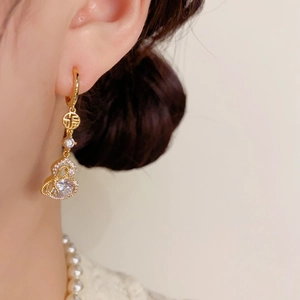 Détail de boucles d'oreilles hulu dorées avec nœud en zircon et caractère fu sur mannequin