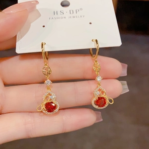 Détail de boucles d'oreilles gourde dorées avec zircon rouge et motif du signe Fu