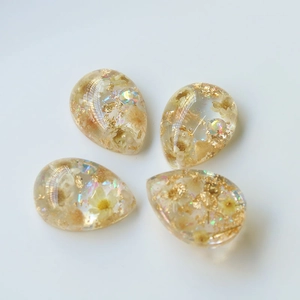 Dettaglio macro di ciondoli a goccia in resina con fiori secchi e foglie d'oro