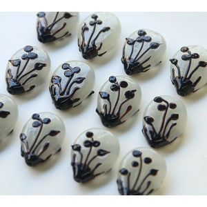 Detailed view of oval glass beads with artistic ink flower patterns and hole drillings
