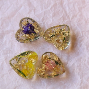 Macro shot of resin heart charms with embedded dried flowers and gold leaf foil
