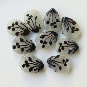 Detailed view of eight teardrop-shaped glass beads with brown floral ink patterns