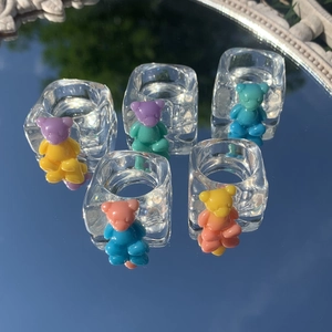 Detailed macro view of five transparent resin rings with colorful bear charms on a mirror