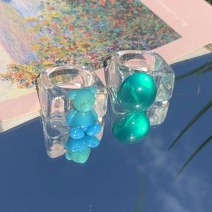 Detail shot of acrylic square rings with blue bear and green gem on reflective surface