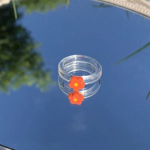 Detail eines transparenten Harzrings mit oranger Blume auf einer Spiegelfläche
