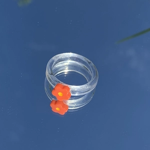 Detail eines transparenten Harzrings mit oranger Blume, gespiegelt auf Glas