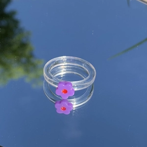 Nahaufnahme eines klaren Harzrings mit violetter Blüte auf einem spiegelnden Hintergrund