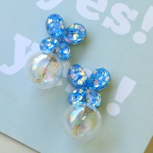Detalle de pendientes de mariposa de resina azul con lentejuelas y colgante de bola iridiscente