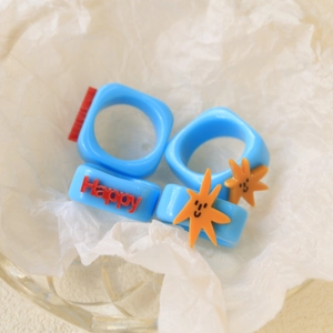 Close-up of blue acrylic rings featuring red Happy lettering and orange star charm