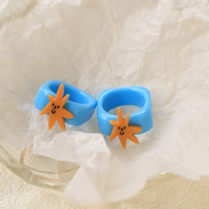 Detail of blue resin starfish rings with orange smiley face on wrinkled paper