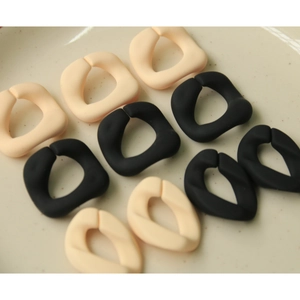 Nahaufnahme matter geometrischer Acryl-Kettenglieder in Schwarz und Creme auf Keramikteller