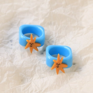 Close-up of blue resin square rings featuring a yellow happy face starfish design