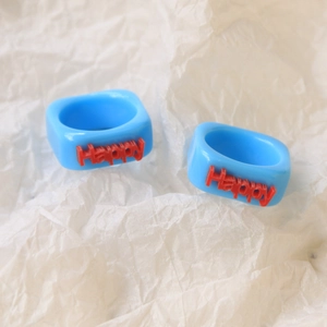 Detail of two light blue square resin rings with red Happy letter embossed design
