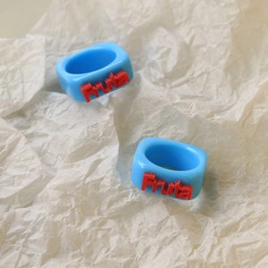 Detail of blue resin rings with 3D red Fruta letters in a Y2K dopamine style