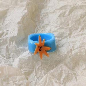 Close-up of a blue resin square ring featuring an orange starfish smile face design