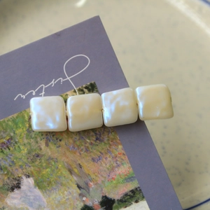 Détail de perles carrées crème sur une barrette à cheveux posée sur une carte rétro