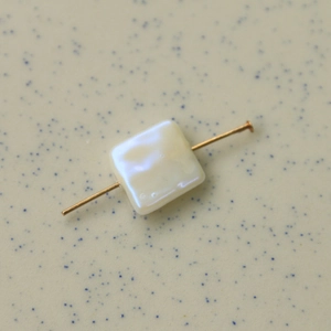 Gros plan sur une perle carrée nacrée avec tige dorée pour bijoux faits main