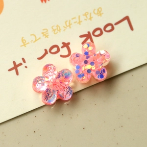 Macro shot of two pink resin flower charms with colorful sequins for DIY crafts