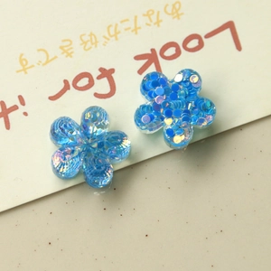 Close-up of two blue resin flower charms with sparkling sequins for DIY jewelry making