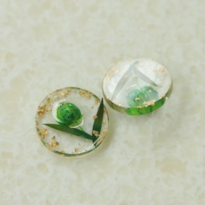 Détail de breloques rondes en résine avec fleurs séchées vertes et feuilles d'or pour bijoux