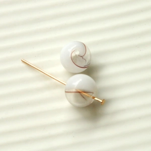 Macro detail of 16mm gradient glass beads with reddish swirls and gold jewelry pins