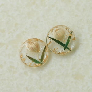 Détail de breloques rondes en résine avec fleurs séchées roses et feuilles d'or