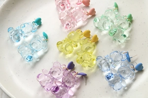 Detail of candy-colored gummy bear earrings with frosted heart studs on ceramic tray